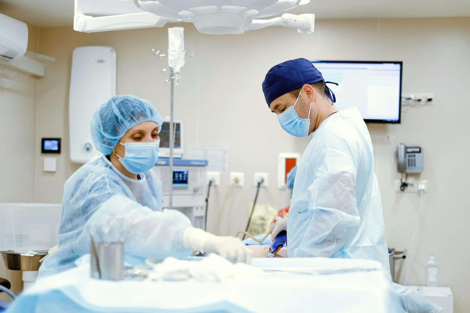 Two surgeons in protective gowns and masks performing a medical procedure in a bright, modern operating room.